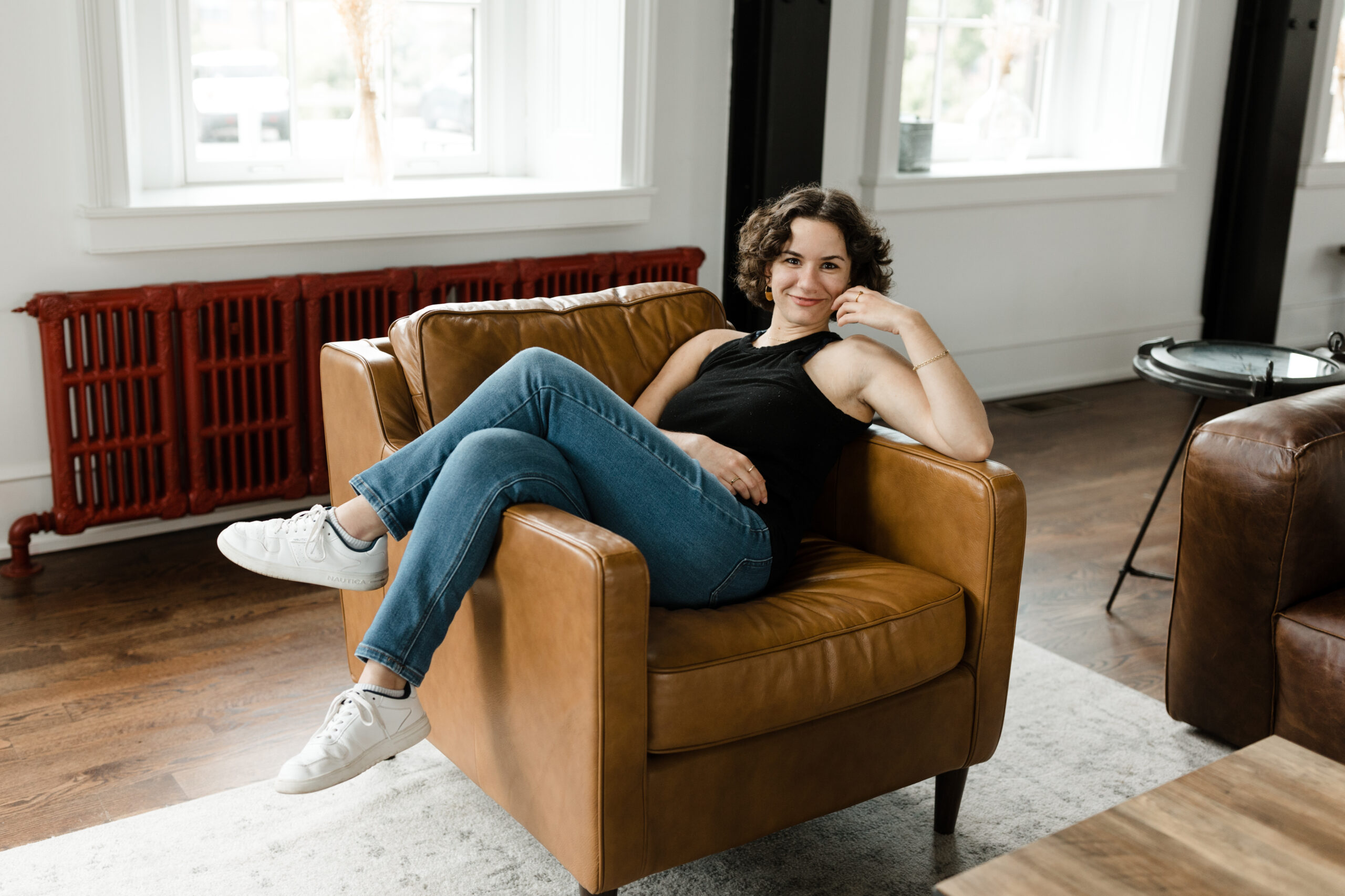A wedding copywriter sits sideways in an oversized leather chair