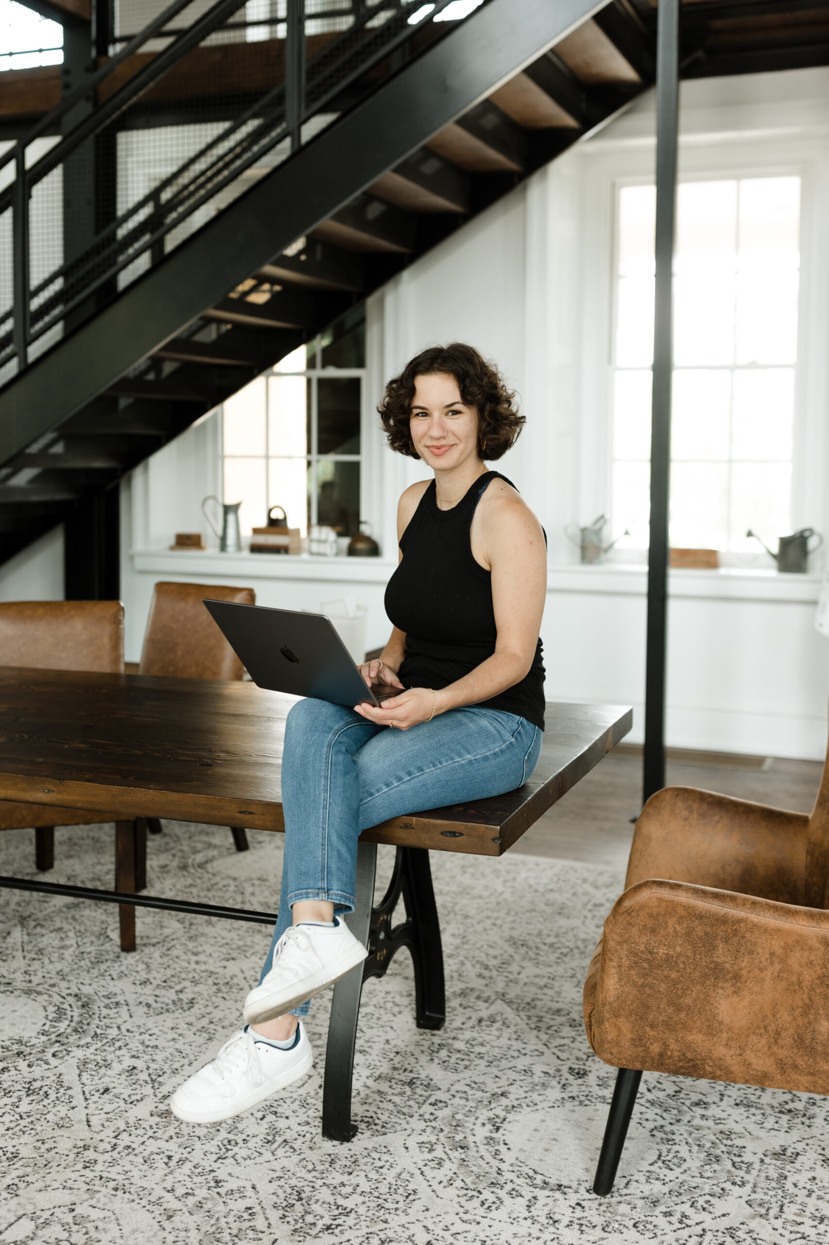 A young woman sits on a table with a laptop in her hands