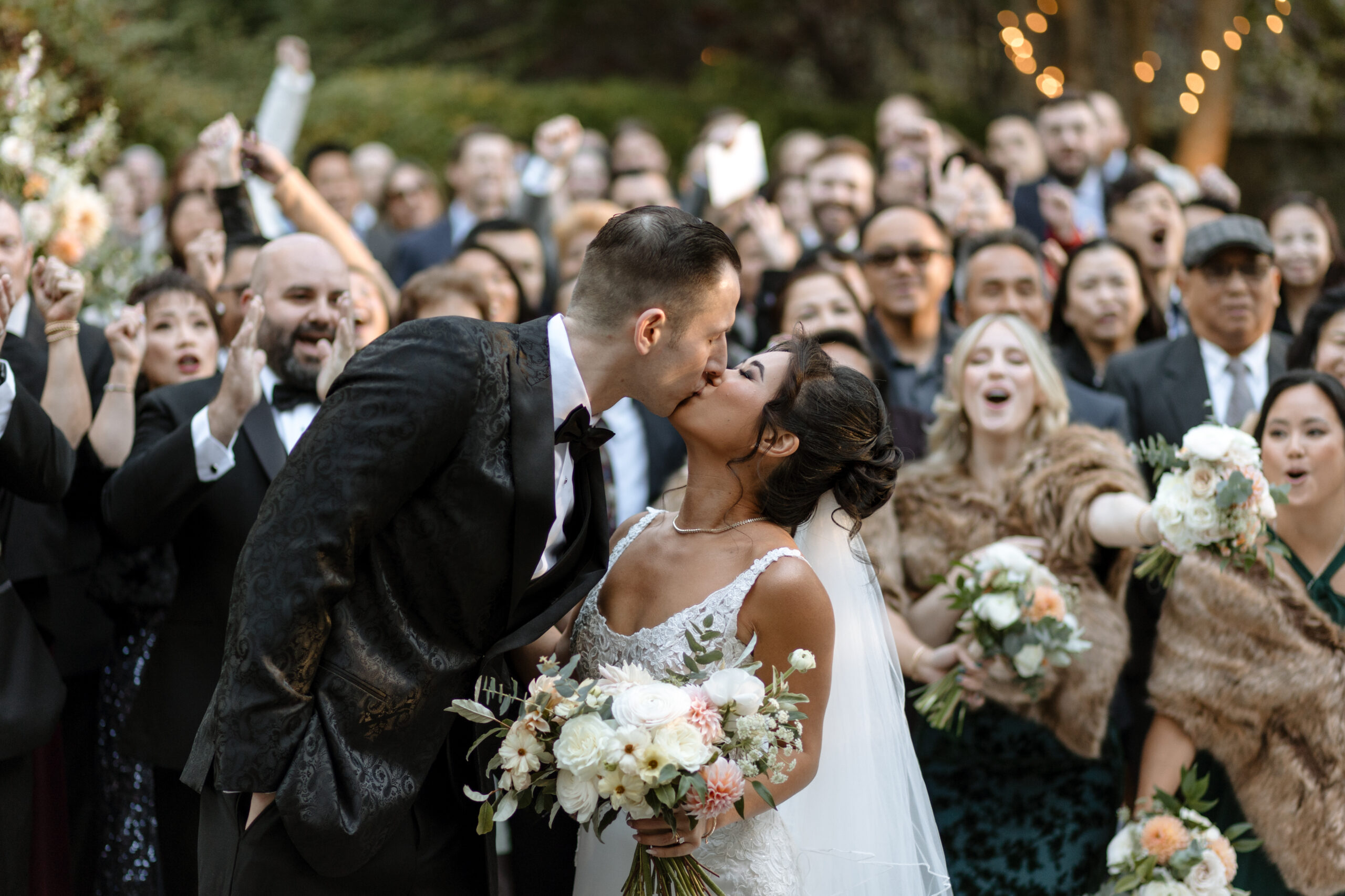 A bride and groom kiss surrounded by their wedding party 