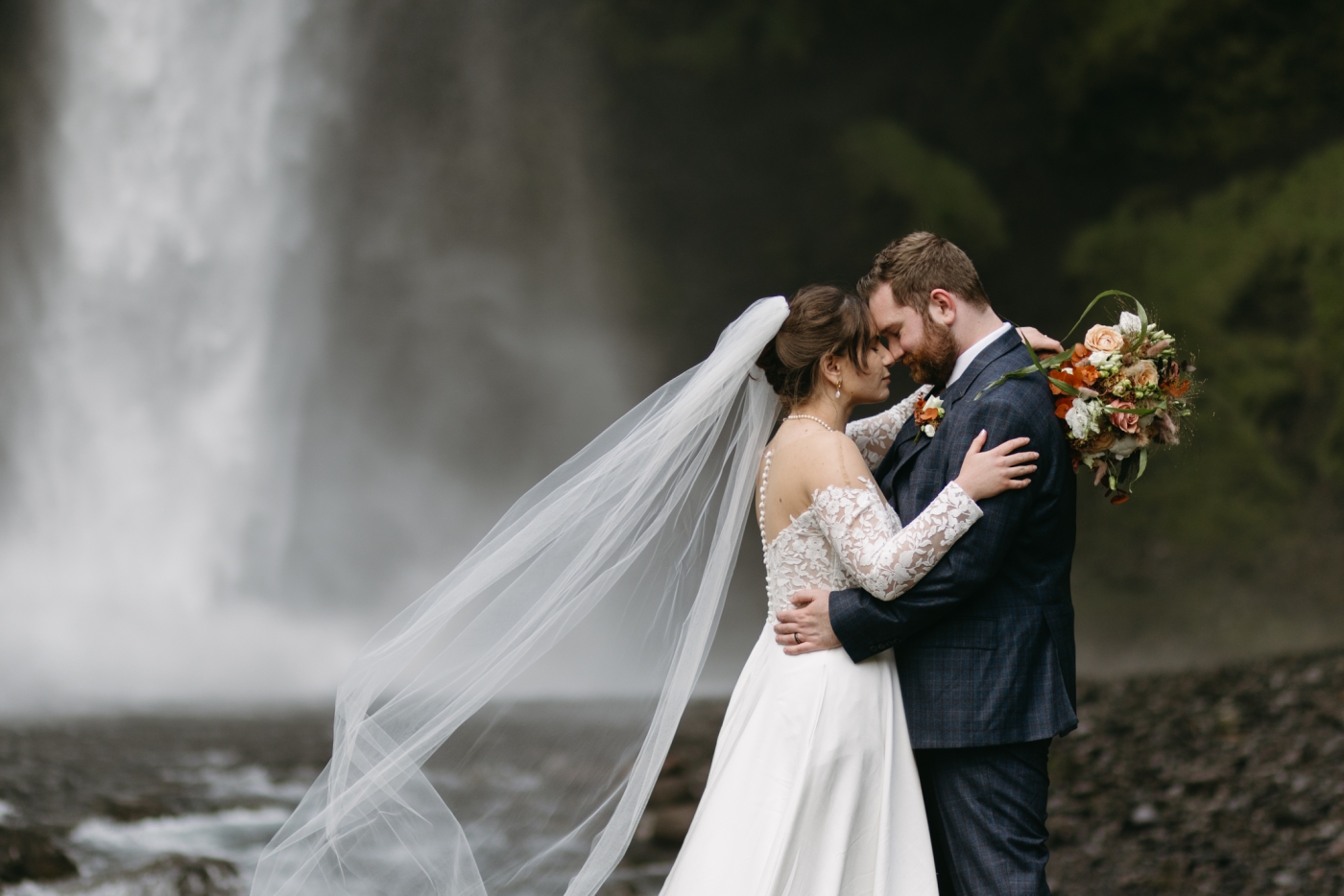 A bride and groom touch their foreheads together at Kvernufoss